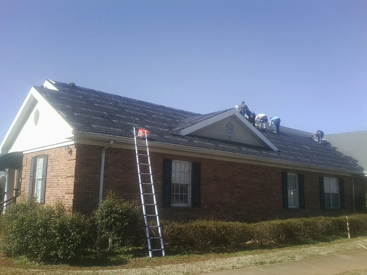 Crew tearing shingles off a brick ranch roof with a ladder set — Metal Roof Repair work by our crew in Emlenton