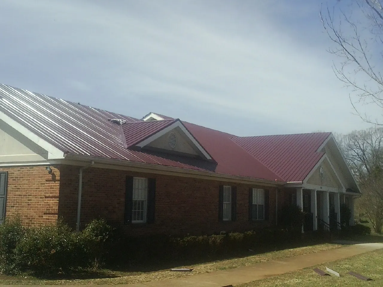 Red metal roof with gabled entries on a long brick building, from a Hail Damage Roof Repair job in Emlenton