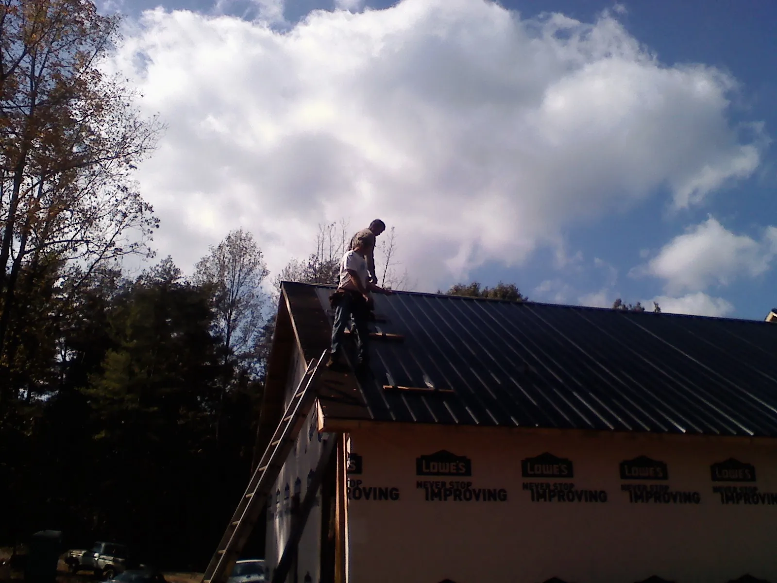Roofer fastening dark metal panels high against a cloudy sky, from a Roof Inspection job in Emlenton