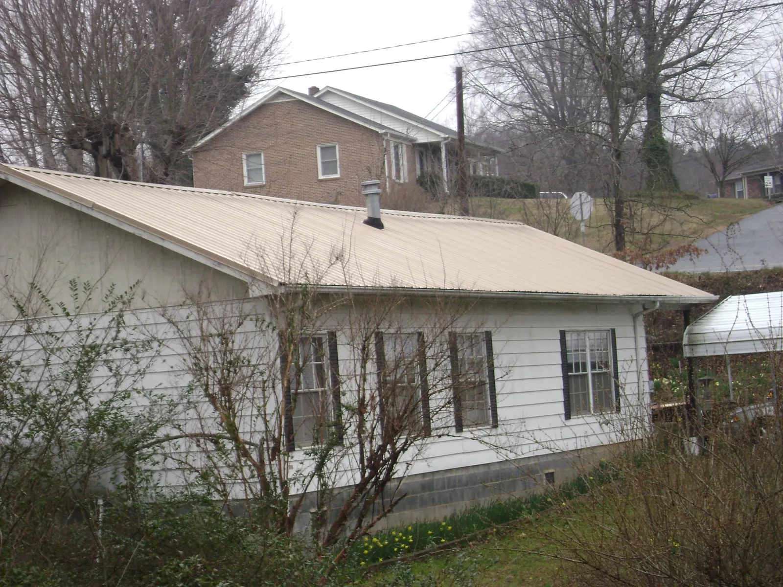 Tan metal roof on a white sided house set into a hillside — Commercial Roofing by Roofing Brothers in Emlenton